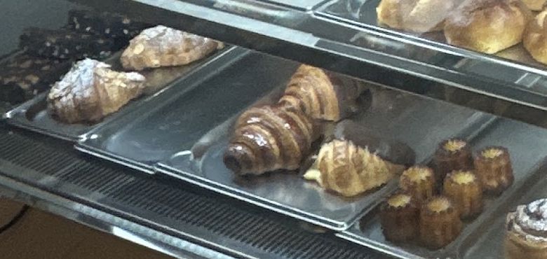 Croissante și prăjituri mici aranjate pe tăvi în vitrina Chocolatine&Co
