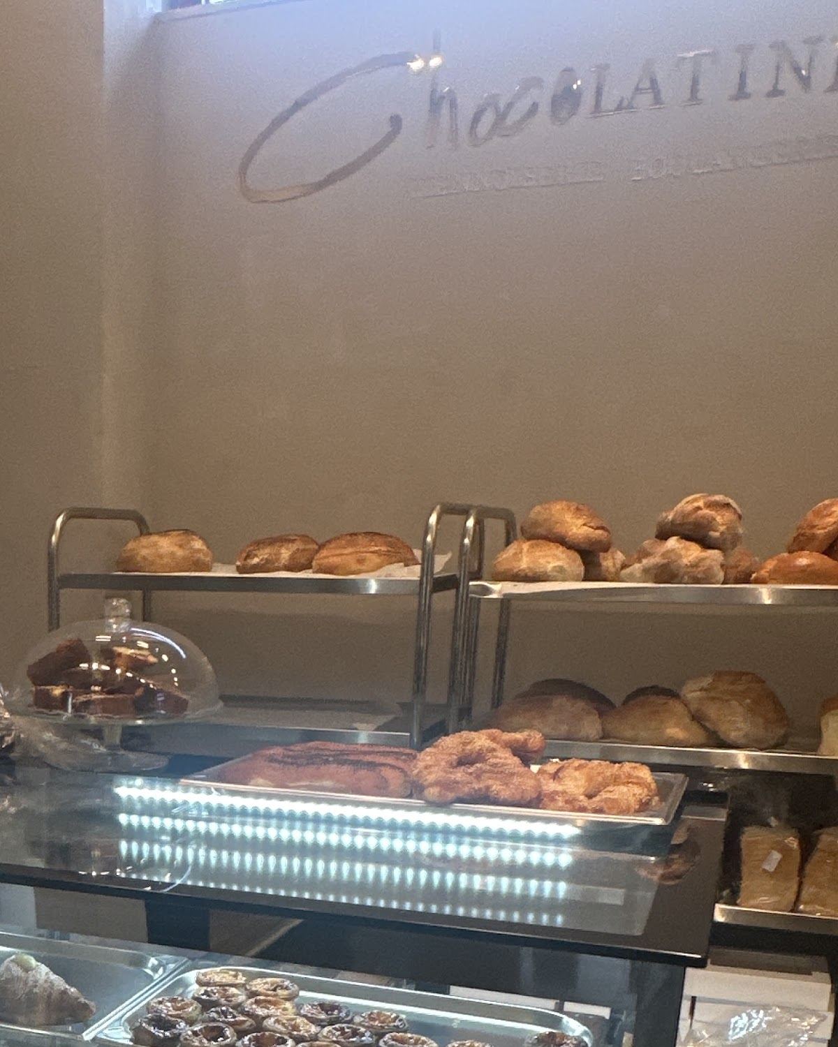 Logo-ul Chocolatine&Co pe peretele din spatele tejghelei, deasupra rafturilor cu pâine