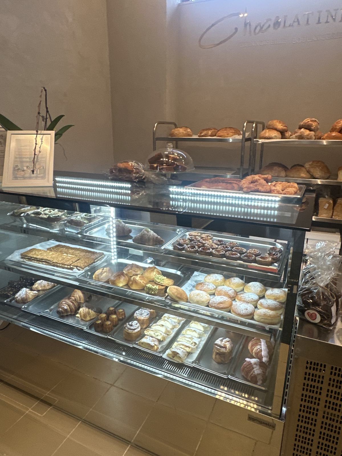 Vitrina Chocolatine&Co cu croissante, gogoși, prăjituri și pâini pe rafturi, cu logo-ul pe perete